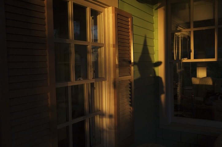 A silhouette of a witch against a green house in a Halloween-themed photo.